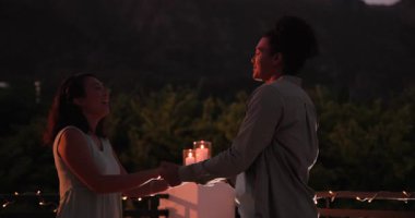 Çatı katındaki balkonda sicim lambalarının altında birbirine sarılan farklı çiftler. Bu arada adam yüzük kutusuyla evlenme teklif ediyor. Romantizm, kutlama, yakınlık, zarafet, ortam, bağlantı, mutluluk