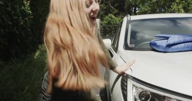 Beyaz SUV 'de mavi fiyonk gördükten sonra, kadın garaj yolunda yürüyor, kapıyı açmadan önce kontrol ediyor. Kutlama, beklenti, hediye, sürpriz, mutluluk, açık hava, modern