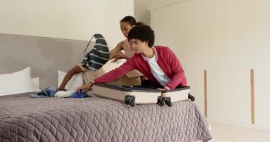 Çeşitli aileler yataklarına bavullarını topluyor, evde neşeli ifadelerle tatile hazırlanıyorlar. Seyahat, hazırlık, valiz, neşe, heyecan