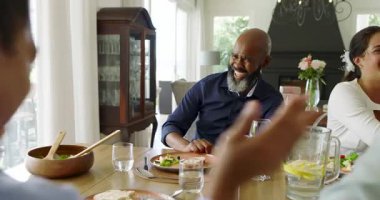 Olgun bir siyahi hikaye anlatıcısı, gülüşmeler ve ahşap masanın etrafındaki aileyle bir şeyler paylaşma anı. Aile, toplantı, etkileşim, kutlama, birliktelik, sıcaklık, zarafet.