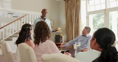 Kıdemli adam ödülü tutuyor, çeşitli arkadaşlar evde kutlama yaparken gülümsüyor. Başarı, takdir, alkış, mutluluk