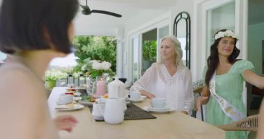 Çeşitli kadın grupları verandada toplanıyor. Akıllı telefon özçekimi çekiyorlar. Fotoğrafları gözden geçiriyorlar. Kutlama, dostluk, zarafet, açık hava, rahatlık, sıcaklık, samimiyet.