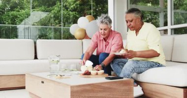 Son sınıf arkadaşları doğum gününü parlak bir verandada kutluyor, tatlı tabağını ahşap masaya koyuyorlar. Kutlama, dostluk, açık hava, neşeli, tatlılar, veranda, canlı, toplanma, mutluluk