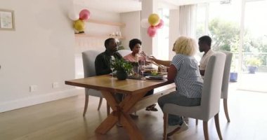 Çeşitli arkadaşlar evde, güzel bir şekilde hazırlanmış yemek masasında birlikte gülüp eğleniyorlar. Arkadaşlık, yemek, toplanma, kutlama, sofra kurma, kahkaha