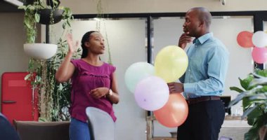 Afrika kökenli Amerikalı çift ofis doğum gününü renkli balonlar ve ofis bitkileriyle kutluyor. Kutlama, çift, neşe, ofis, doğum günü, coşku, dekor