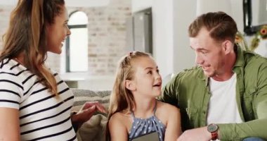 Baba kanepede kızına selam verirken anne ultrason gösterip evde bebek haberlerini paylaşıyor. Aile, annelik, beklenti, neşe, bağlantı, kutlama, modern