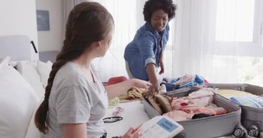 Asyalı bir kadın otel odasında kontrol listesini tutarken Afro-Amerikalı bir kadın bavulunu topluyor. Paketleme, seyahat, arkadaşlık, hazırlık, otel, yaşam tarzı, macera, organizasyon