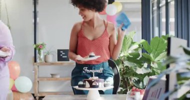 Çeşitli iş arkadaşları renkli balonların arasında ofiste veda pastası dağıtıyorlar. Kutlama, takım çalışması, parti, ofis, neşe, nostalji, jest