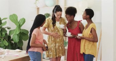 Çeşitli bayan arkadaşlar çaylarını yudumlarken telefonda hamile kadınlara kek ikram ederken gülüyorlar. Arkadaşlar, kutlama, annelik, sosyal toplantı, mahrem, kadınsı, neşe