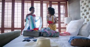 Tatil için hazırlanan çeşitli kadın çiftler heyecanlı bir şekilde evlerinde güneşli yatak odalarında kıyafet seçiyorlar. Seyahat, hazırlık, giysi, yaşam tarzı, arkadaşlık, moda