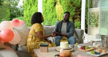 Doğumgününü dışarıda kutlayan Afro-Amerikan çift, pasta ve hediyelerle birlikte. Kutlama, neşe, birliktelik, şenlikler, hediyeler, tatlı