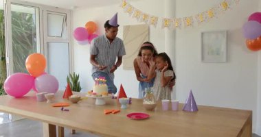 Çeşitli aileler doğum günü evlerini kutluyor, kek, şapka ve balonlarla neşe içinde gülüyorlar. Kutlama, neşe, pasta, renkli, parti, aile, birliktelik, heyecan
