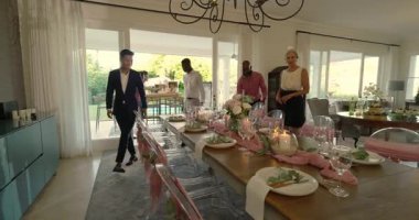 Ev sahibi hareketin ardından, çeşitli arkadaşlar yemek odasına giriyor, pembe kuşaklı koltuklarda oturuyorlar. Zarif, kutlama, topluluk, konukseverlik, samimiyet, kırsal, canlı