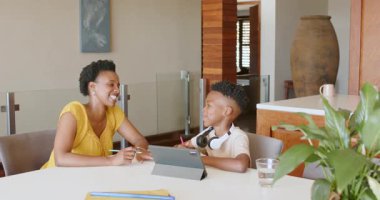 Anne oğluna tablet ödevinde yardım ediyor, baba telefonda konuşuyor. Aile, teknoloji, dijital, öğrenme, evde eğitim, çoklu görev