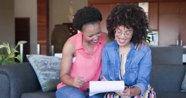 İki farklı kadın çift evlerindeki kanepede neşeyle kucaklaşıyorlar, samimi anlarını paylaşıyorlar. Arkadaşlık, bağ, mutluluk, birliktelik, rahatlama, şefkat.