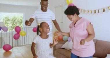 Aile evde kutlama yapıyor, kız kıza dans ediyor, erkek gülümsüyor ve bayram bayrağıyla çömelmiş bir kadın. Kutlama, balonlar, neşe, aile, neşe, dekorasyon, dans