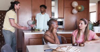 Partide, arkadaşlar modern mutfakta yemeğin tadını çıkarıyor, kahkaha ve sohbeti paylaşıyorlar. Toplanma, yemek, birliktelik, ev, mutfak, kutlama