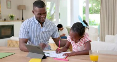 Afro-Amerikalı baba ve kızı aydınlık yaşam evinde tablet ve renkli kağıtlarla meşgul. Neşeli, etkileşimli, rahat, yaratıcı, bağlanma, doğal ışık, aile, canlı