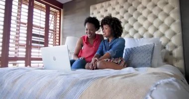 Dizüstü bilgisayarda film izleyen mutlu kadın çift yatak odasında, evde eğleniyor. Aşk, rahatlama, teknoloji, eğlence, birliktelik, ev