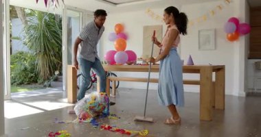 Çeşitli çiftler modern evlerinde süpürge kullanarak konfeti temizliyor, çocuklara ev sahipliği yapıyorlar. Kutlama, temizlik, çift, modern, neşeli, parti, ev