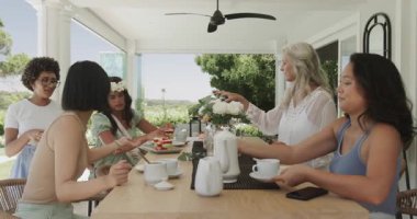 Kıdemli bir arkadaş çaydanlığı kaldırırken çeşitli bayan arkadaşlar verandada çay ve kek dağıtırlar. Arkadaşlık, sosyalleşme, kutlama, neşe, açık hava, boş zaman, kırsal