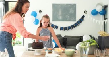 Hediye paketi geliyor, anne ve kız pasta yerleştiriyor, doğum günü atıştırmalıkları hazırlıyor ve masaya sarılıyorlar. Kutlama, aile, birliktelik, sıcaklık, dekor, neşe, hazırlık