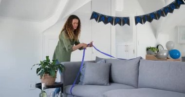 Masaya şarap bardakları koyduktan sonra kadın pasta kurdelesi ve balonlarla doğum günü için evi dekore ediyor. Kutlama, şenlik, zarafet, dekor, konukseverlik, sosyal, iç mekan