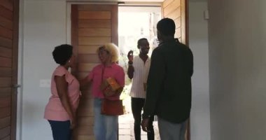 Çeşitli arkadaşlar evde birbirlerini sıcak bir şekilde selamlıyorlar, hediyelerini tutuyorlar ve mutlu bir şekilde gülümsüyorlar. Arkadaşlık, kutlama, mutluluk, hediye, birliktelik, mutluluk.