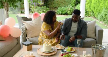 Çiftler açık hava bahçe partisinde pasta ve meyve tabağı yiyor, gülüşlerini paylaşıyorlar. Kutlama, açık hava, tatlı, toplanma, birliktelik, arkadaşlık.