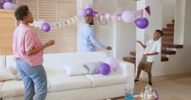 Evde kutlama yapan Afro-Amerikan ailesi balonlarla gülüp dans ediyor. Kutlama, mutluluk, birliktelik, şen, neşeli, parti