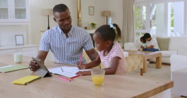 Küçük çocuk gülüyor ve kız yemek masasında tableti paylaşırken gülümsüyor. Aile, sıcaklık, etkileşim, işbirliği, yaratıcılık, samimiyet, birliktelik, ev