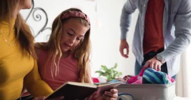 Çeşitli aile kucaklaşması ve bavulları paylaşıyor. Kızları yatak odasında tablet sayfaları gösteriyor. Aile, kaynaşma, birliktelik, aile içi, yaşam tarzı, neşeli, samimi