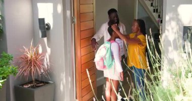 Afro-Amerikan ailesi evde saçlarını okul için düzleştiriyor, sırt çantasını ayarlıyor, sarılıp vedalaşıyor. Aile, ebeveynlik, sabah rutini, banliyö, destekleyici, şefkatli, neşeli