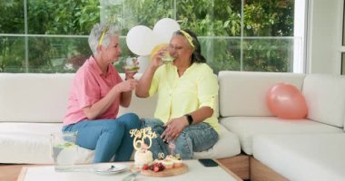 Farklı son sınıf arkadaşları 60. yaş gününü rahat oturma odasındaki kanepede pasta yiyerek kutluyorlar. Doğum günü, kutlama, dostluk, rahat, toplanma, sevinç, rahatlama, yaşam tarzı