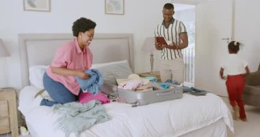 Açık havadar bir evde, yatağın yanına gri bavul hazırlayan yetişkin bir kadın. Çocuk da onu izliyor. ev, paketleme, aile, seyahat, organizasyon, doğal ışık, minimalizm, bağ