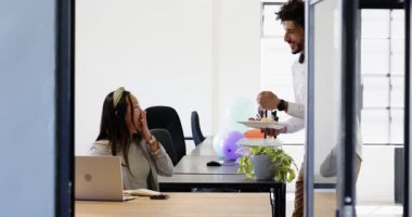 Modern ofisteki iş kadınına mum ve balonla pasta getiren mutlu bir iş adamı. Ofis partisi, eğlence, kutlama, iş, ofis ve iş ortamı kavramı.