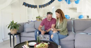 Olgun bir çift doğum günü kutlaması hediye kutlarken erkekler evde kanepede kolye takıyor. Romantizm, kutlama, neşe, samimiyet, samimiyet, şefkat, dostluk