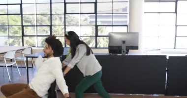 Mutlu iş arkadaşları ofiste eğleniyor, kadın modern ofiste ofis sandalyesinde adamı itiyor. İş, iletişim, iş, ofis çalışma ortamı kavramı.