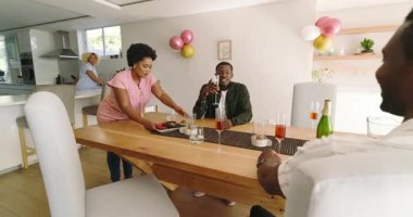 Çeşitli arkadaşlar evde yemek masasının etrafında içki içip sohbet etmekten zevk alıyorlar. Sosyalleşme, toplanma, arkadaşlık, kutlama, yaşam tarzı, rahatlama