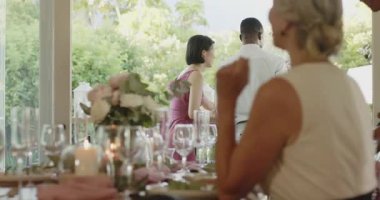 Çeşitli arkadaşlar ev sahibi selamlaşmasını takip ediyor ve cam kapıların yanındaki yemek masasında oturuyorlar. Samimi, kutlama, zarif, keyifli, açık havada, canlı, sosyal.