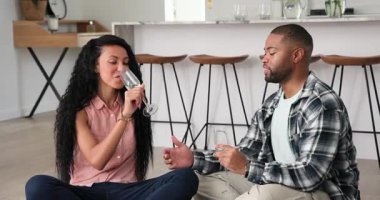 Sohbetten sonra, mutfakta ahşap zeminde oturan, şarap kızartan, çilek besleyen bir çift. Romantizm, samimiyet, kutlama, modern, rahat, yaşam tarzı, arkadaşlık