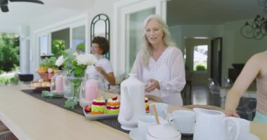 Mini kek tepsisi geldiğinde çeşitli bayan arkadaşlar teras barına şampanya dökerek çaydanlıkları düzenliyorlar. Arkadaşlar, kutlama, brunch, açık hava, neşe, zarafet, birliktelik