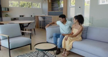 Modern yaşam evinde sohbet eden çeşitli çiftler, yuvarlak kahve masasının yanında ellerinde bir alet tutuyorlar. Modern, parlak, etkileşim, yaşam tarzı, iç mekan, sohbet, günlük mobilyalar, yeşillik