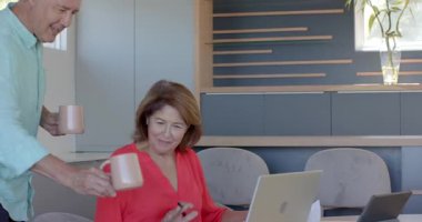 Üst düzey bir çift, mutfak masasında kahve fincanı uzatıp dizüstü bilgisayarı inceliyor, kutlama yapıyorlar. Aile, arkadaşlık, işbirliği, yaşam tarzı, modern, neşeli, konfor