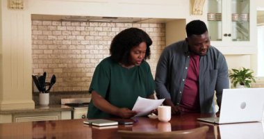 Afro-Amerikalı çift mutfak masasında dizüstü bilgisayar ve kahveyle mali konuları tartışıyor. Bütçe, tartışma, aile, planlama, takım çalışması