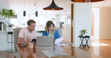 Evde başarıyı kutlayan bir çift, dizüstü bilgisayarın yanında sevinçle kağıt sallıyor. Kutlama, takım çalışması, başarı, mutluluk, teknoloji, uzaktan çalışma