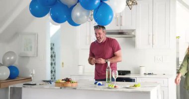 Aperatifleri ayarlarken ve adada şarap dökerken sarkmayı fark eden çift balonları ayarlıyor. Kutlama, dostluk, konforlu, rahat, keyifli, modern, evcil