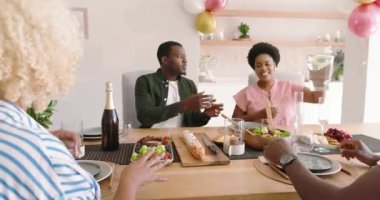 Çeşitli arkadaşlar evde öğle yemeğinin tadını çıkarıyor, kahkahalar ve sohbetler ediyorlar. Arkadaşlık, kaynaşma, sosyalleşme, yemek, mutluluk, evde yemek.