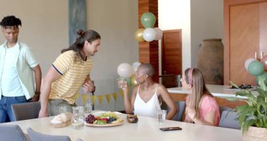 Partide, masanın etrafında toplanmış, arkadaşlar abur cubur ve içecekleri paylaşıyor, birlikte gülümsüyorlar. Kutlama, arkadaşlık, birliktelik, parti, mutluluk, keyif