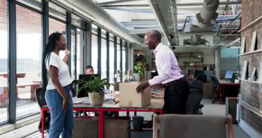 Çeşitli iş arkadaşları modern ofis alanlarında yürüyor, masada karton kutunun yanından geçiyor ve kutluyorlar. Meslektaşlar, işbirliği, etkileşim, kutlama, modern, kurumsal, takım çalışması